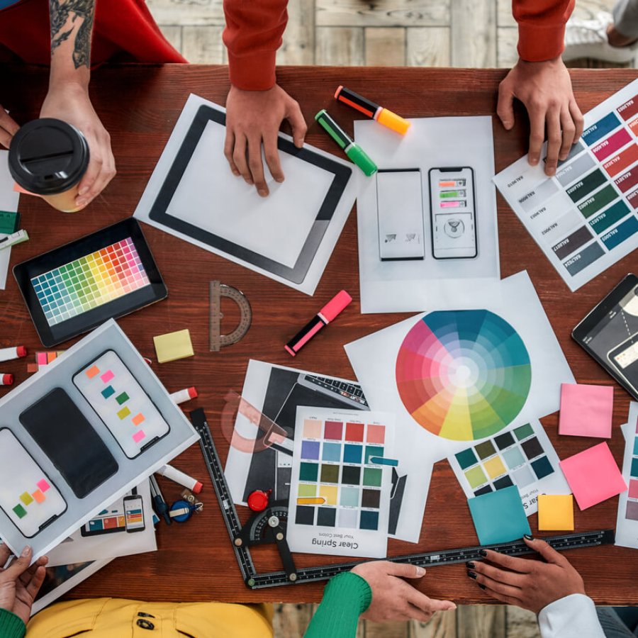 Working on a new project together. Top view of designers discussing sketches, choosing colors from palettes lying on the desk while having a meeting in the modern office Top view of designers discussing sketches, choosing colors from palettes lying on the desk while having a meeting in the modern office. Creative agency concept. Web design. Teamwork